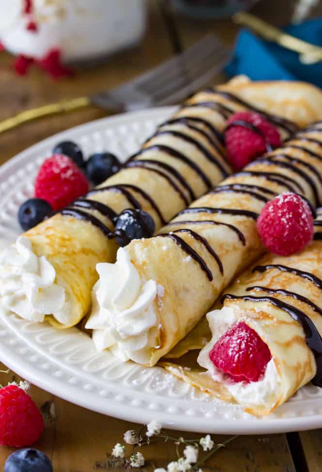 Crepes recipe filled with whipped cream and topped with berries, powdered sugar, and chocolate